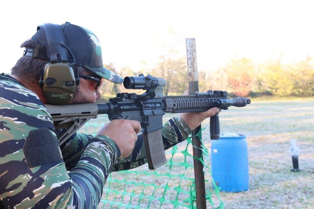 Competitor in camouflage aiming a rifle at an outdoor shooting range