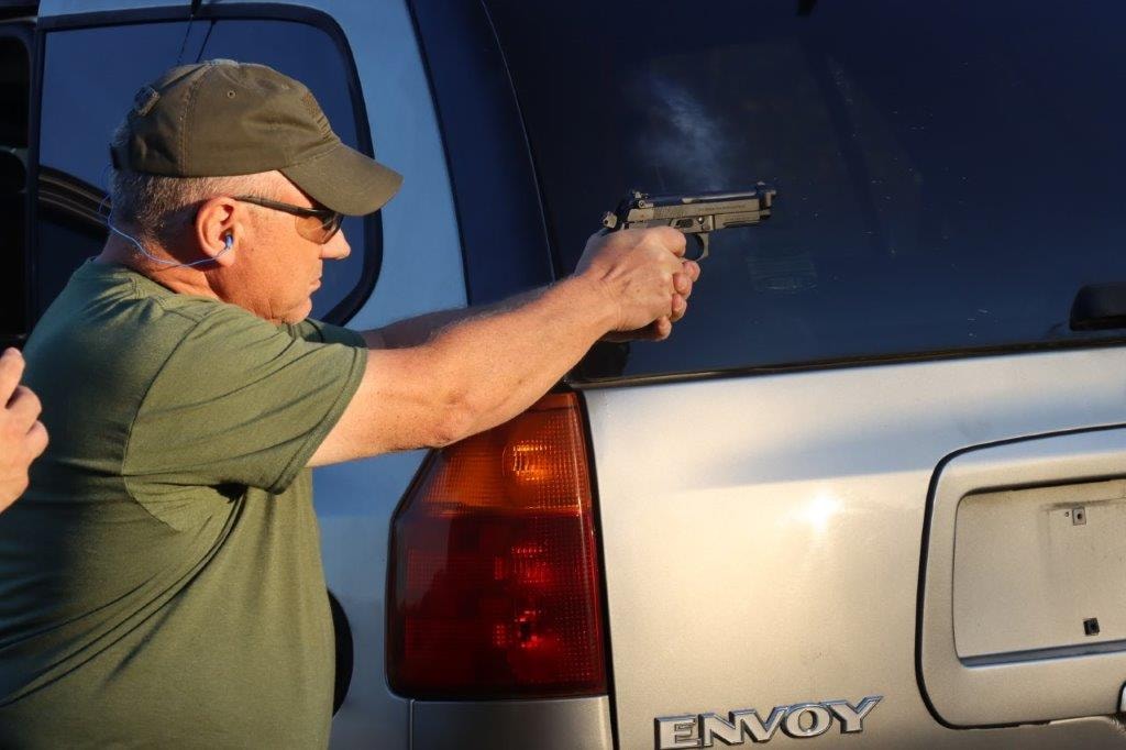 Competitor aiming a handgun beside a vehicle at the range